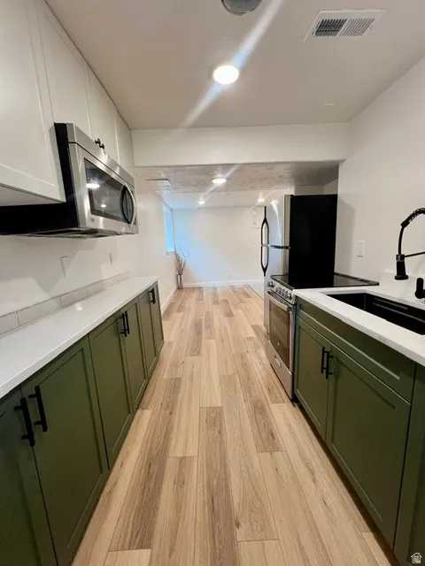 Kitchen featuring wood-finish flooring, two-tone cabinetry with matte black hardware, white countertops, and stainless steel appliances