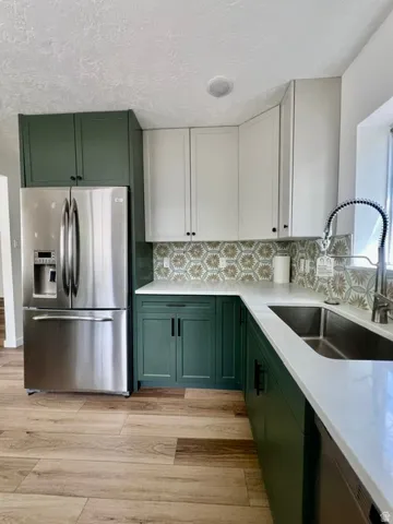 Modern kitchen featuring two-tone cabinetry, stainless steel refrigerator, patterned tile backsplash, white countertops, and wood-finish flooring