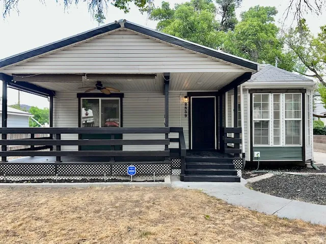 Exterior featuring light-colored siding with dark trim, a covered porch with a ceiling fan, black railings, a bay window with a shingled roof, and a dark entry door