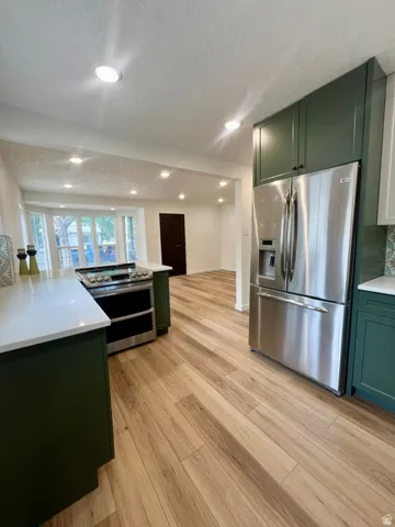 Kitchen featuring wood-finish flooring, stainless steel appliances, dark green cabinetry, white countertops, and recessed lighting