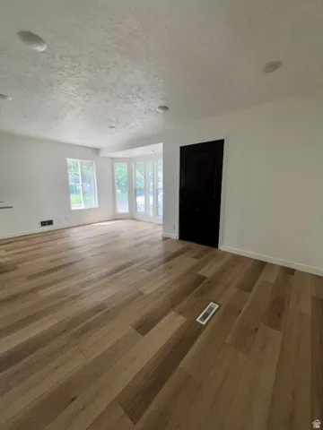 Spacious room featuring wood-finish flooring, white walls, and a textured white ceiling with recessed lighting