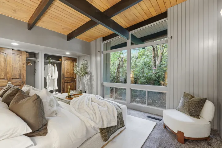 Primary bedroom featuring a wood-panel ceiling with exposed beams, full-height window, vertical paneled wall, recessed lighting, and wood doors
