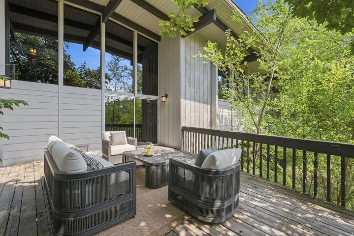 Expansive wood deck with a dark wood railing, surrounded by mature trees