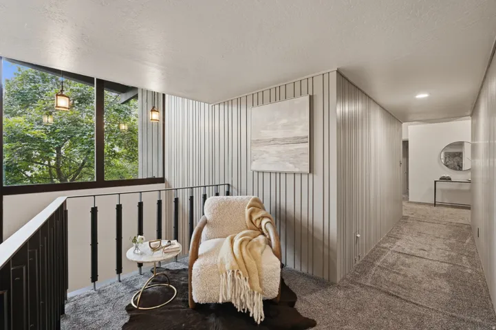 Upper-level landing featuring a large picture window, a black metal railing, and light-toned vertical paneling