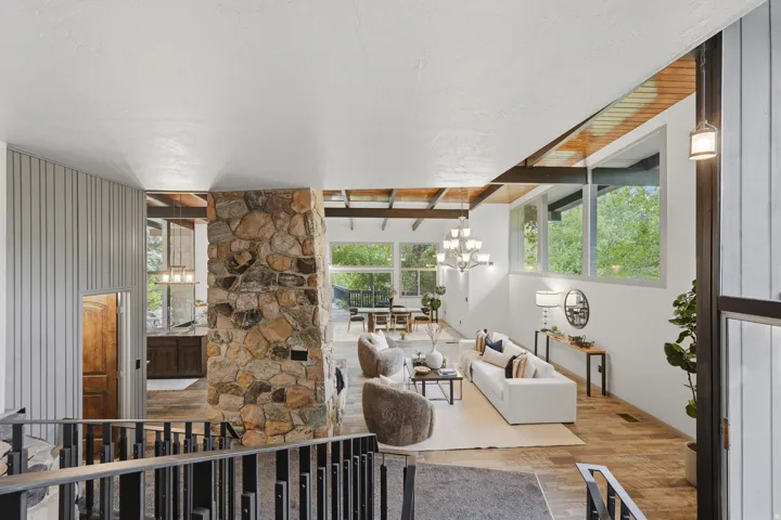 Foyer overlooking the expansive living area featuring a floor-to-ceiling stone fireplace, interior waterfall, exposed wood beam ceilings, and large windows