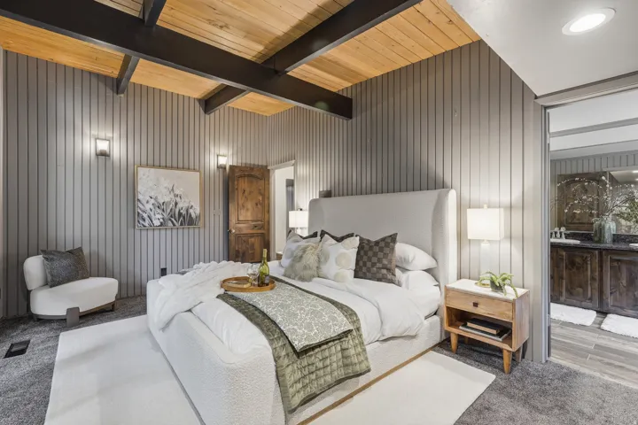 Bedroom featuring a wood-panel ceiling with exposed beams, vertical slat wall paneling, and wall sconce lighting. Entrance to the ensuite bathroom.