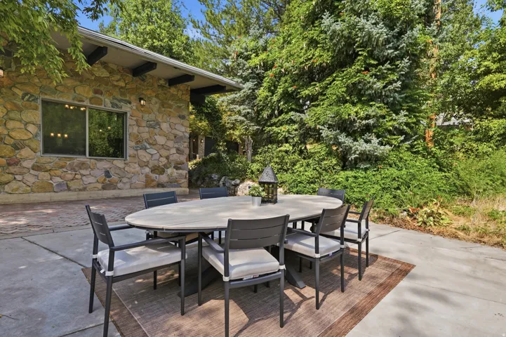 Expansive concrete patio with a decorative area rug, surrounded by mature trees and lush landscaping