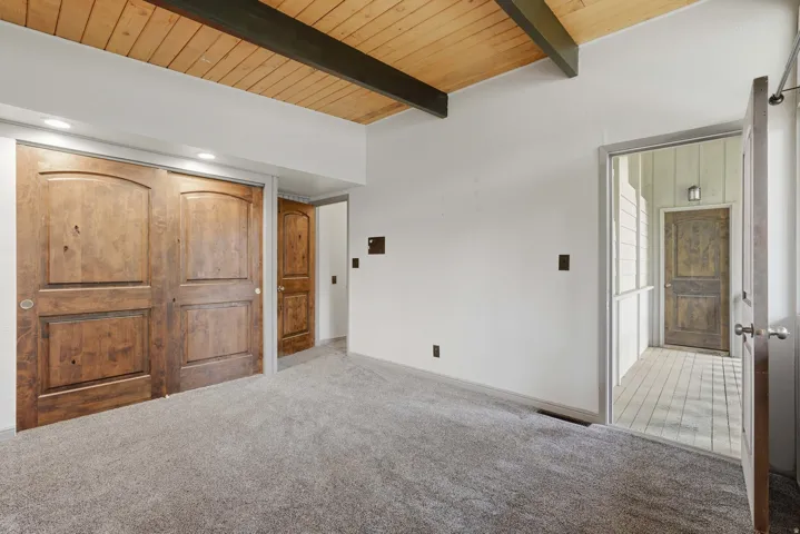Carpeted room featuring a vaulted wood-paneled ceiling with exposed beams, recessed lighting, and a double sliding wood-paneled closet door
