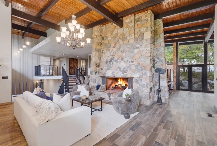 Expansive living space featuring a large pass-through stone fireplace, a 2-story waterfall, and a natural wood plank ceiling with exposed beams