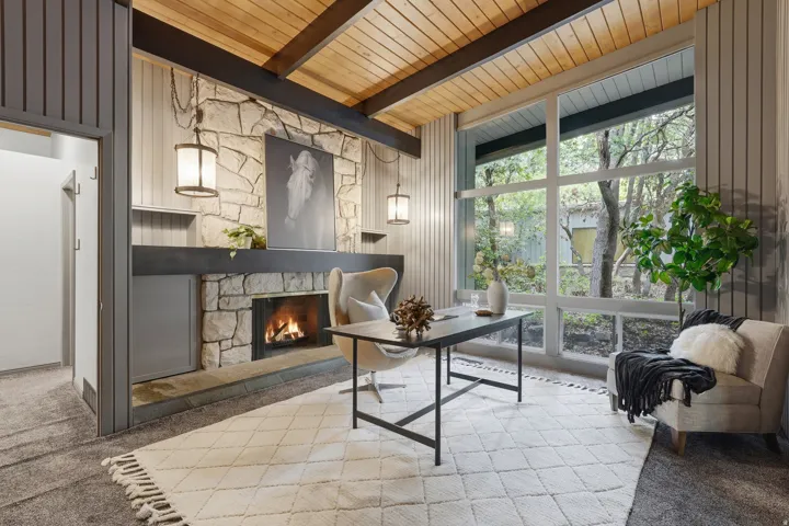 Stone fireplace with hearth, wood-paneled ceiling, exposed wood beams, and a large window wall
