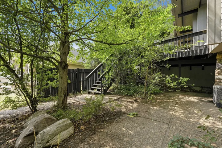 Expansive outdoor area featuring a mature tree, natural rock landscaping, and a multi-level wood deck with stairs leading to the upper level