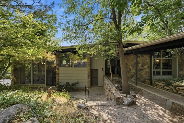 Stone and siding exterior with expansive windows, a covered walkway, and a paved entry ramp