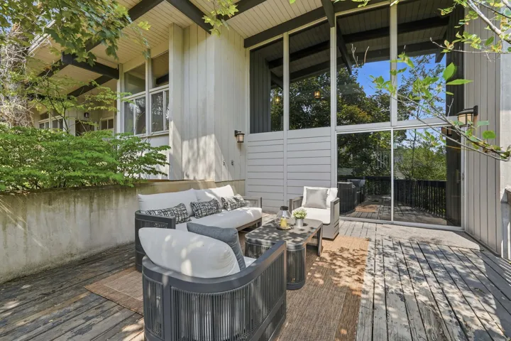Expansive exterior deck featuring wood-finish flooring, a full-height glass wall, and modern wall-mounted lighting
