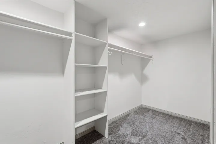 Walk-in closet featuring built-in shelving, dual hanging rods, recessed lighting, and textured carpeting