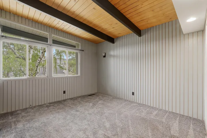 Vaulted wood plank ceiling with exposed beams, textured vertical paneling, and broad windows featuring transoms