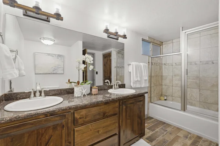 Spacious bathroom featuring a dual vanity with a dark wood-finish cabinet and stone-finish countertop