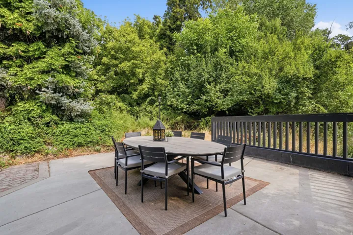 Expansive outdoor patio featuring a concrete surface, bordered by mature trees and lush landscaping
