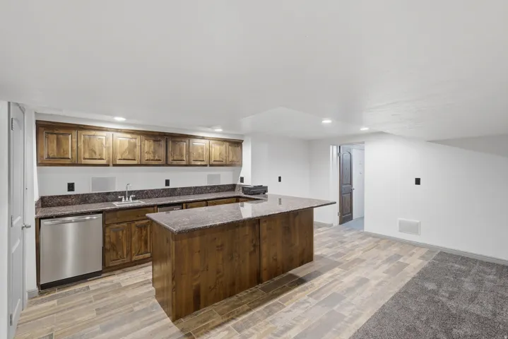 Built-in wet bar featuring wood cabinetry, a granite countertop, undermount sink, and stainless steel dishwasher