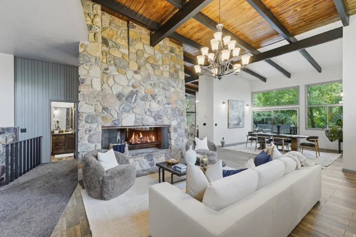 Great room featuring a floor-to-ceiling stone fireplace, exposed wood beam ceilings, a formal dining area and close access to powder bath