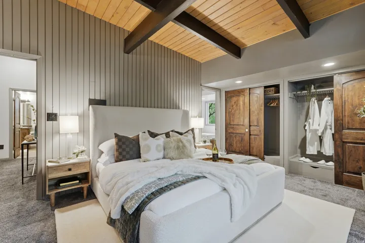 Slanted wood-finish ceilings with dark exposed beams, vertical paneled accent wall, and built-in closet storage with wood-finish sliding doors