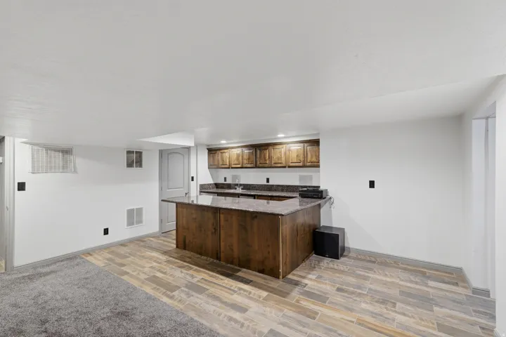 Entertainment area featuring a built-in wet bar with wood cabinetry and a stone countertop. Surround sound speakers are integrated into the ceiling with included sound equipment.