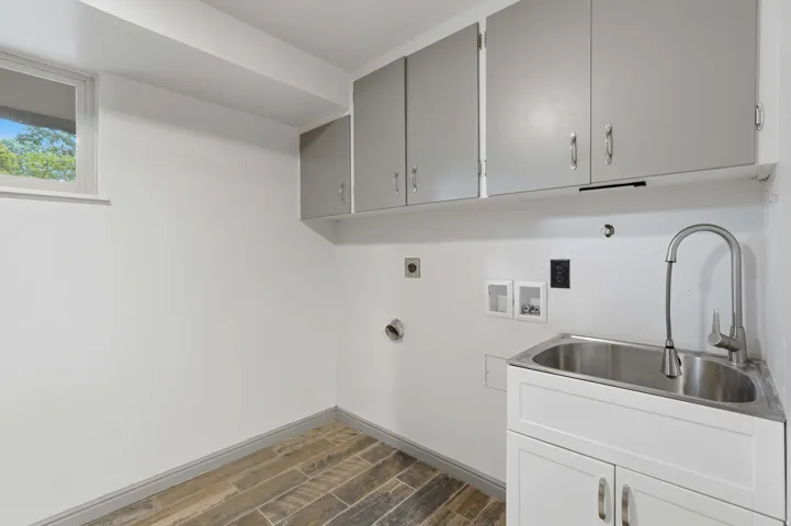 Utility room featuring a stainless steel sink with a gooseneck faucet, white base cabinetry, and gray upper cabinetry