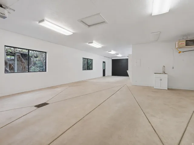 Spacious utility room featuring concrete flooring with integrated drainage, multiple windows, and extensive overhead fluorescent lighting