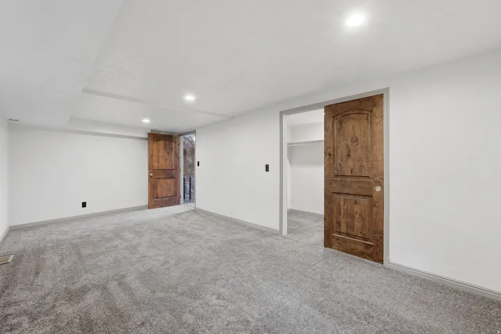 Spacious room featuring gray carpeting, light walls, recessed lighting, and rich wood-finish doors