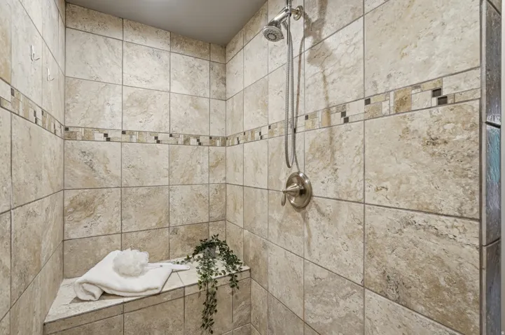 Tiled shower with a built-in bench, brushed nickel fixtures, and a decorative mosaic accent band