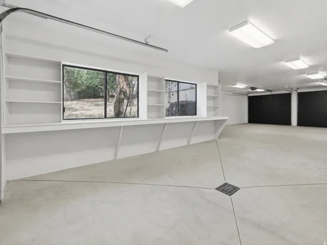 Spacious garage featuring concrete flooring with floor drain, built-in shelving, work surface, and dual windows