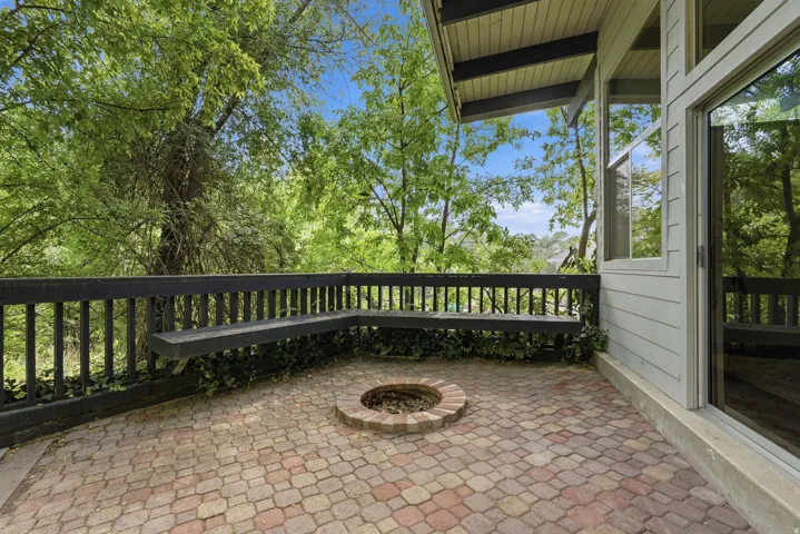 Brick paver patio with a built-in fire pit, surrounded by a wood railing and integrated bench seating
