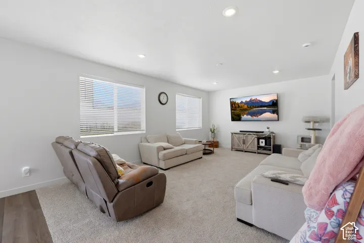 Spacious room featuring light-colored carpeting, multiple windows with blinds, recessed lighting, and a partial wood-finish flooring border