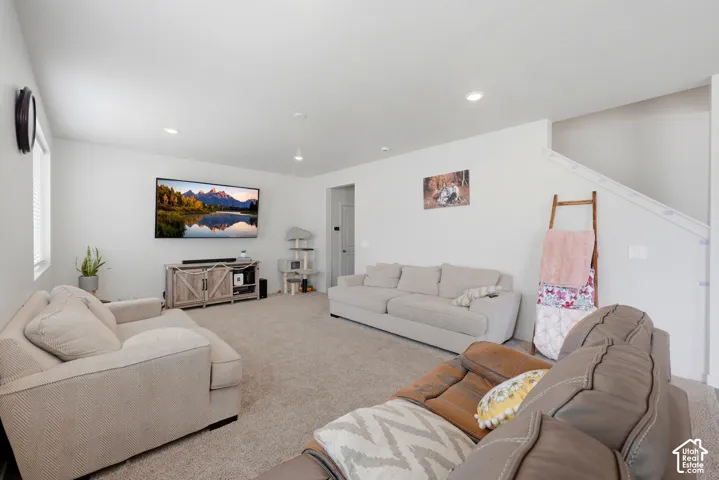 Spacious living area featuring neutral carpeting and light-toned walls, recessed lighting, and a window with horizontal blinds