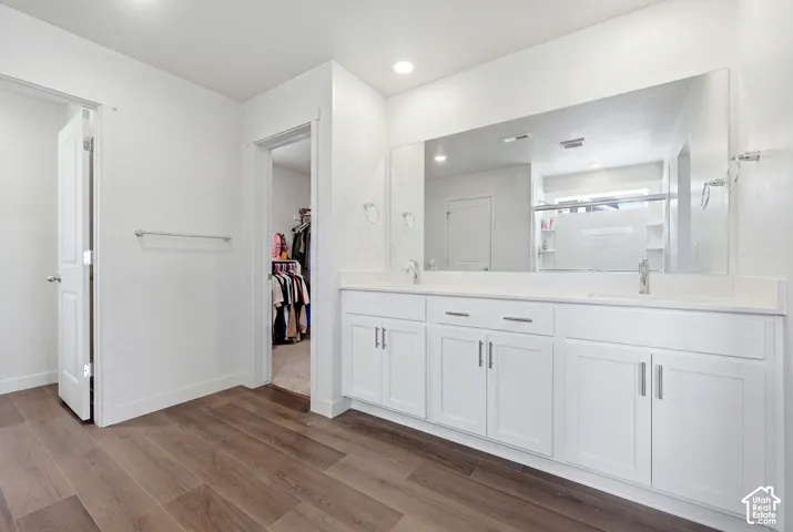 Bathroom featuring a dual vanity with white cabinetry, a large wall-mounted mirror, and wood-finish flooring