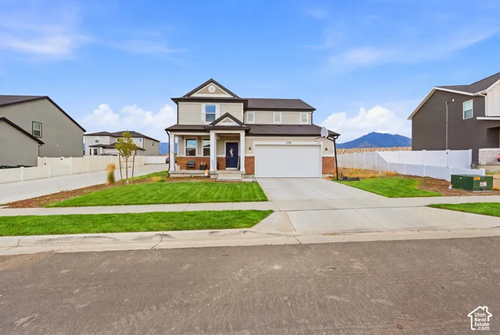 Two-story residential property featuring a light-toned exterior with dark trim accents, a covered front porch, and an attached two-car garage