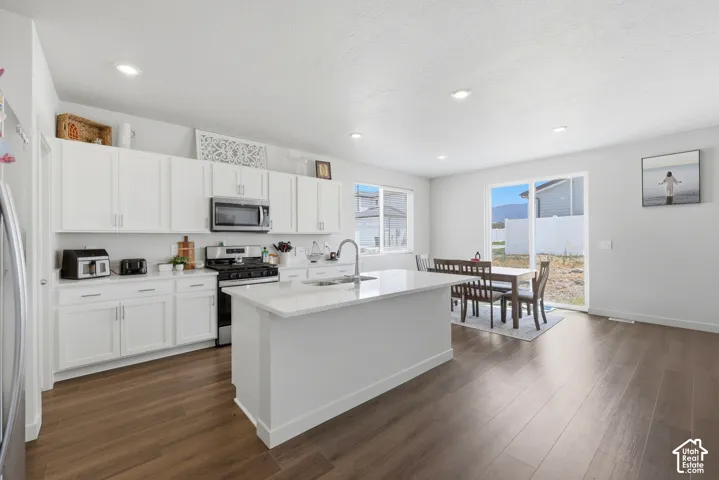 Open-concept kitchen and dining area featuring white cabinetry, stainless steel appliances, a center island with sink, and wood-finish flooring
