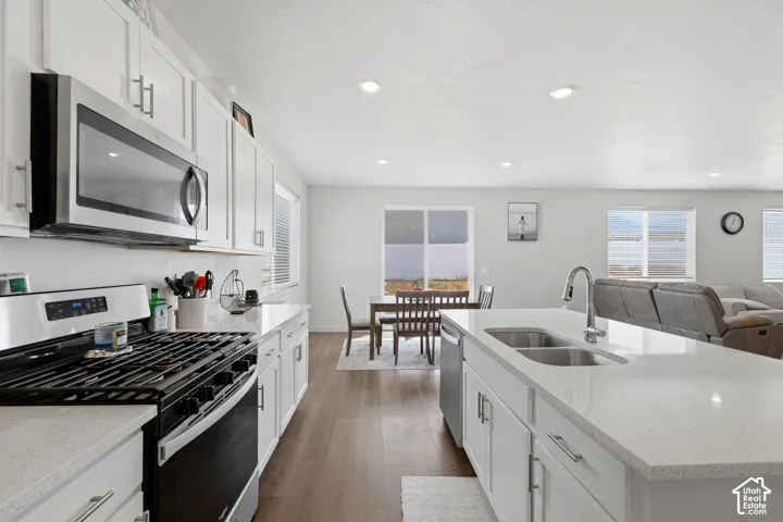 Modern kitchen featuring white cabinetry, stainless steel appliances, light-toned countertops, a gas range, and a kitchen island with an undermount double-basin sink