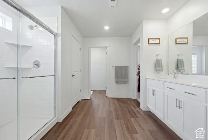 Spacious bathroom featuring a glass-enclosed shower with subway tile surround, a dual vanity with white cabinetry and a light-colored countertop, and wood-finish flooring