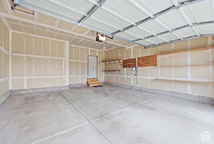 Spacious garage featuring a concrete floor, overhead garage door, built-in shelving, an interior access door, and an automatic garage door opener