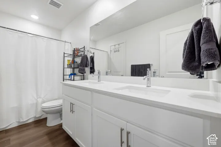 Spacious bathroom featuring a dual vanity with white cabinetry and integrated sinks, a large wall-mounted mirror, wood-finish flooring, and a white shower curtain rod