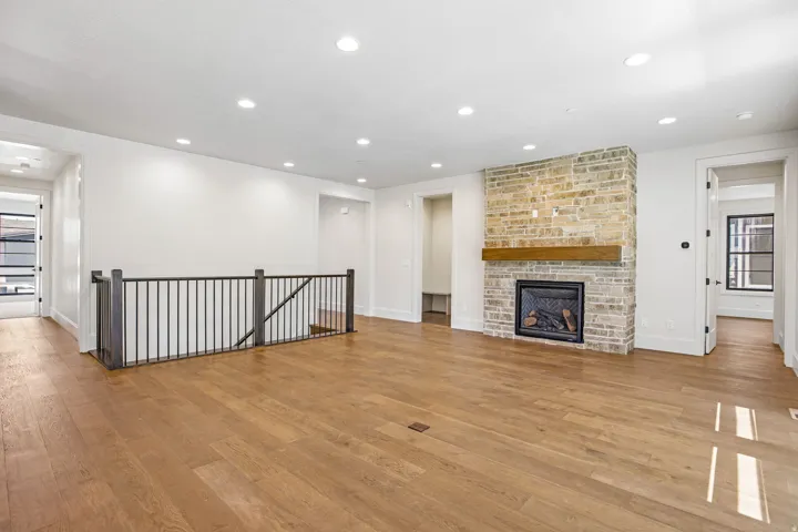 Expansive living area featuring wood-finish flooring, a stone-clad fireplace with a wood mantel, recessed lighting, and a wrought iron railing