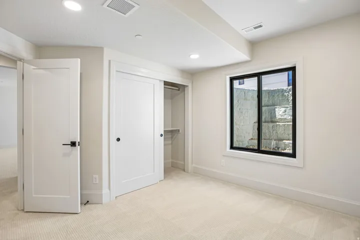 Carpeted room featuring a double-pane window with black framing, a built-in closet with sliding doors, recessed lighting, and a neutral color palette