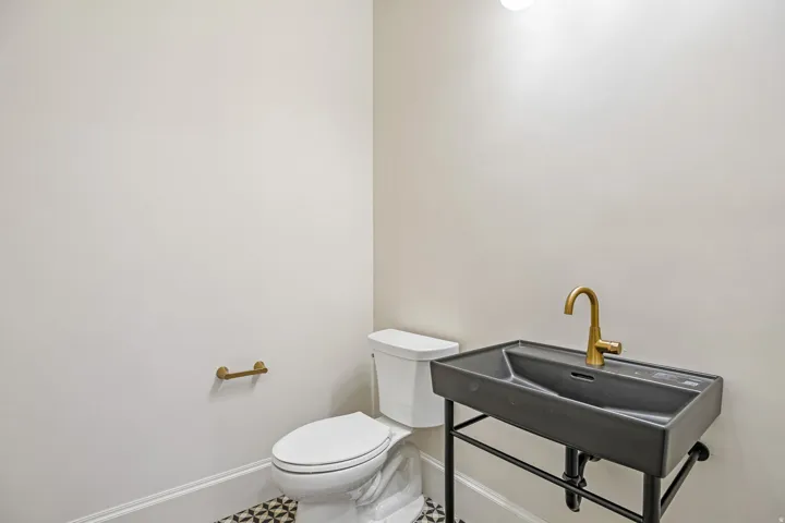 Modern powder room featuring a black vessel sink with integrated countertop, a brass-finish faucet, and a wall-mounted toilet paper holder