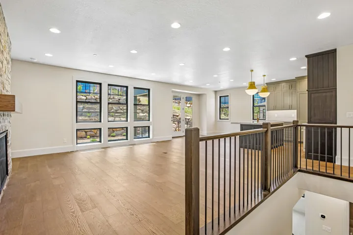 Spacious living area featuring light wood-finish flooring, a stone-clad fireplace, and multiple windows with black frames