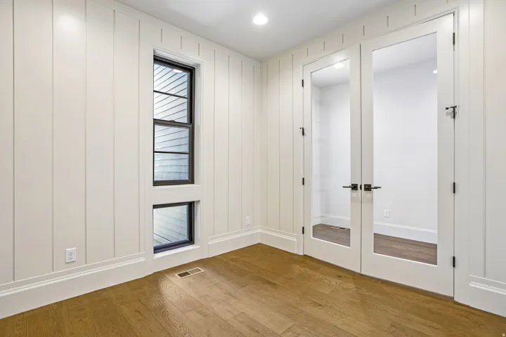Room featuring vertical shiplap wall paneling, a multi-pane window with black trim, and wood-finish flooring