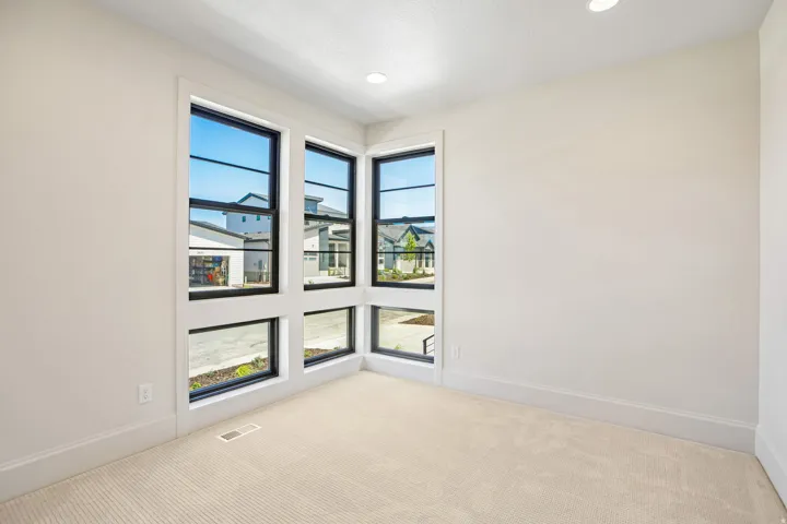 Corner window arrangement with black frames and white trim, recessed ceiling lighting, and neutral-toned carpeting