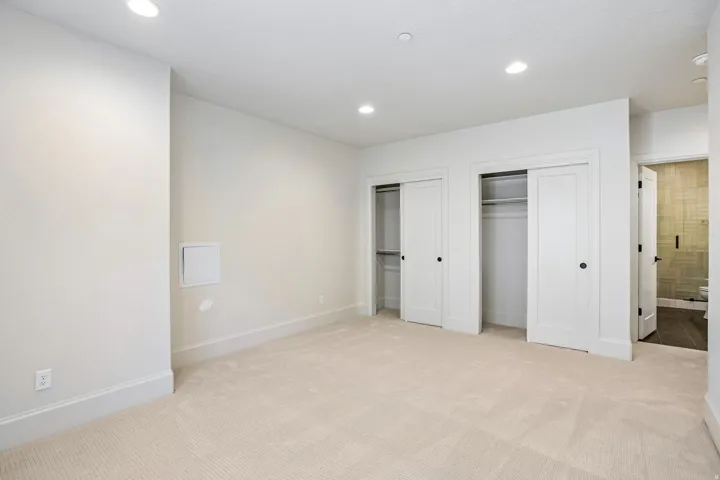 Carpeted room featuring recessed lighting, two closets with sliding doors, white trim, and a doorway to an adjacent tiled area