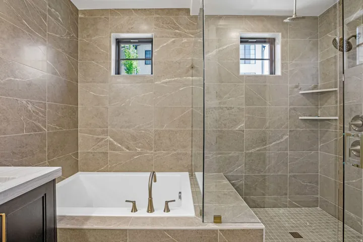 Full tile surround in a neutral tone, featuring a built-in soaking tub with bronze fixtures
