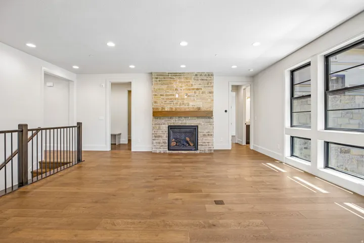 Spacious room featuring wood-finish flooring, a brick-clad fireplace with a wood mantle, and multiple large windows with black frames