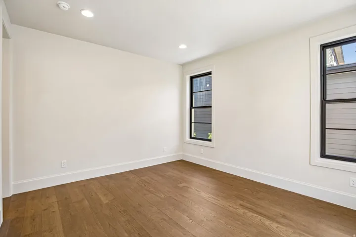 Light-filled interior featuring wood-finish flooring, recessed lighting, crisp white walls, and two modern black-framed windows